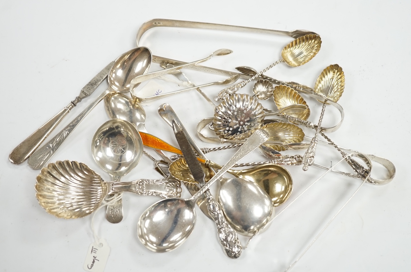 A collection of assorted small silver, sterling and white metal flatware, including two 19th century caddy spoons, enamelled spoon, sifter spoon, teaspoons, sugar tongs, etc. 9oz and two nail implements. Condition - poor